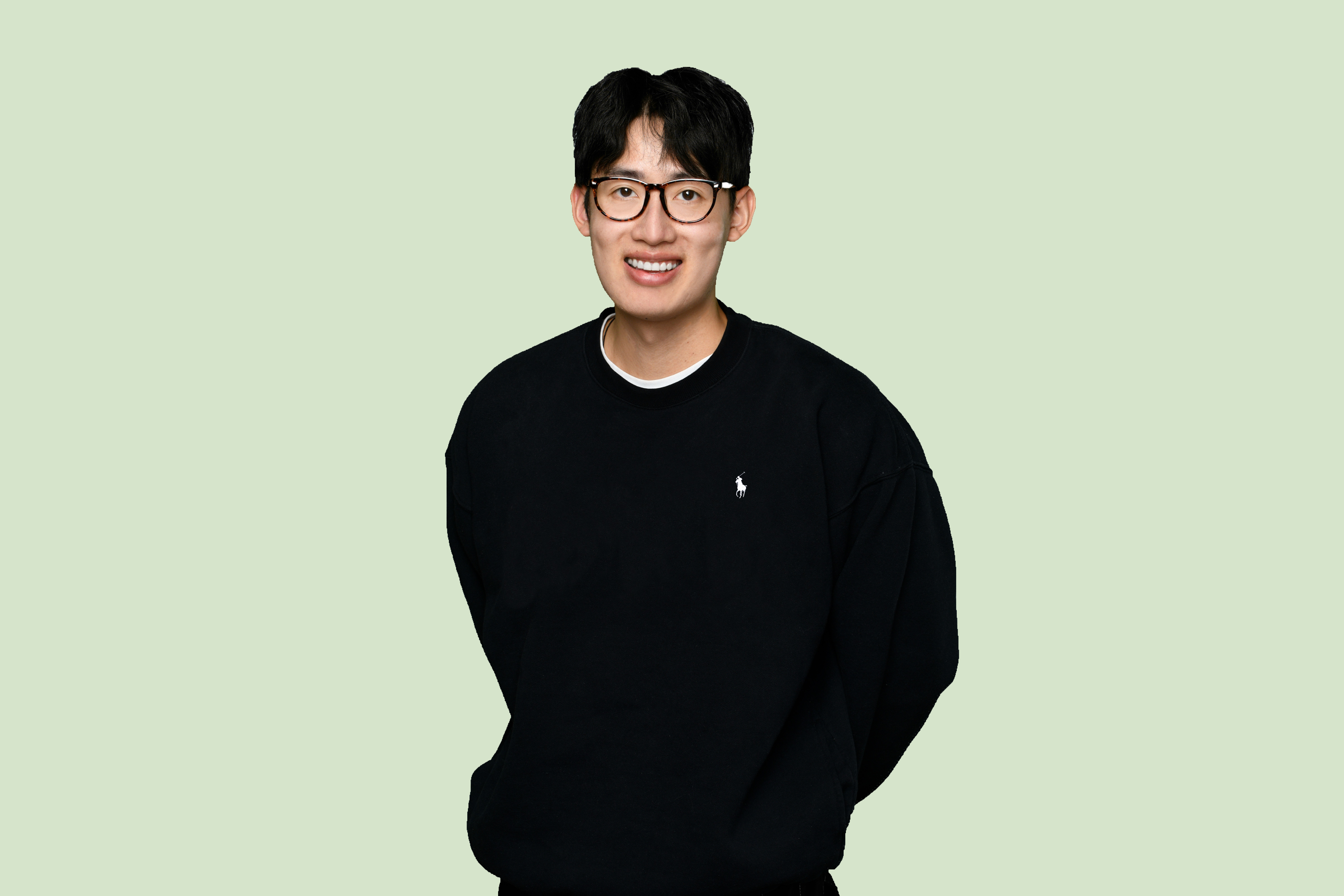 Portrait of a man with brown hair and glasses on a flat gray background.